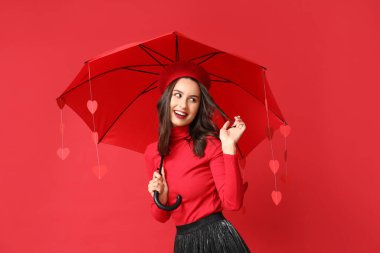 Elinde şemsiyeyle kırmızı arka planda kağıt kalpler tutan güzel bir genç kadın. Sevgililer Günü kutlaması