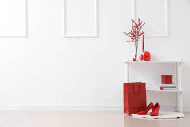 Kırmızı kalp şeklinde hediyesi olan raf ünitesi, alışveriş çantası ve beyaz duvarın yanında ayakkabılar. Sevgililer Günü kutlaması