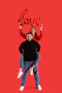 Genç adam kırmızı arka planda kız arkadaşına sırtına biniyor. Sevgililer Günü kutlaması