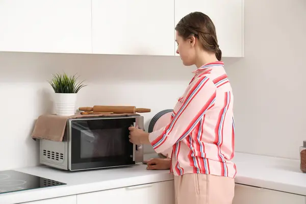 Pretty young woman heating food in microwave oven at home
