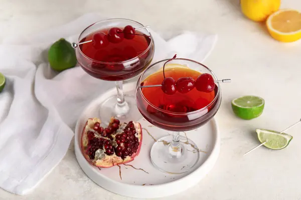 Glasses of Cosmopolitan cocktail with cherries and pomegranate on white background