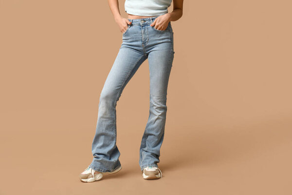 Beautiful young Asian woman in stylish jeans on brown background, closeup