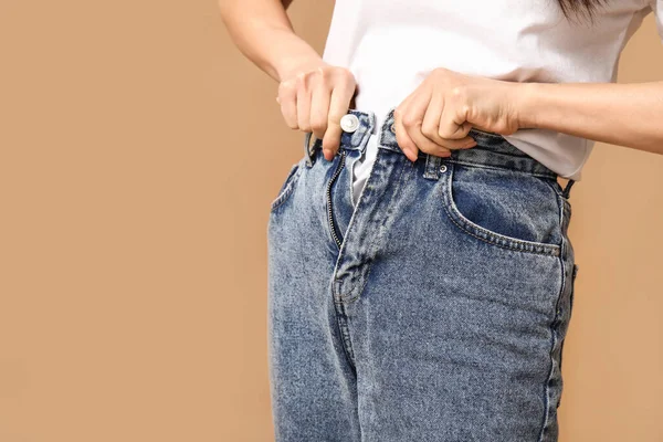 Güzel genç Asyalı kadın kahverengi arka planda şık kot pantolon ilikliyor, yakın plan.