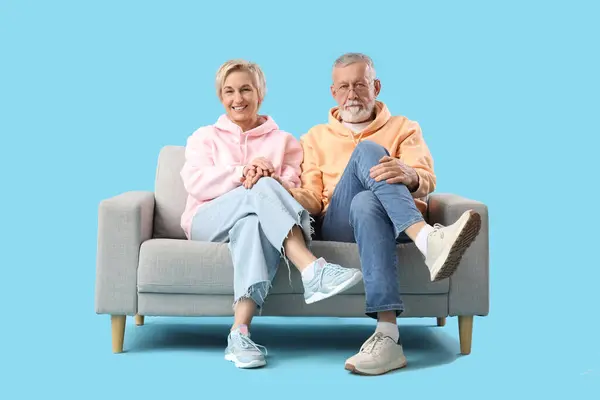 Mature couple sitting on sofa against blue background