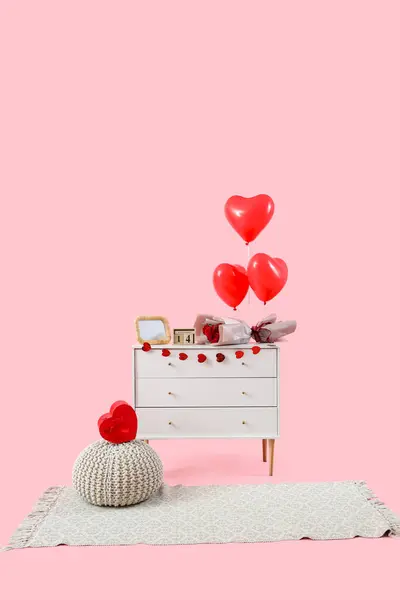 Chest of drawers with heart-shaped balloons, roses and paper heart garland on pink background. Valentine's Day celebration