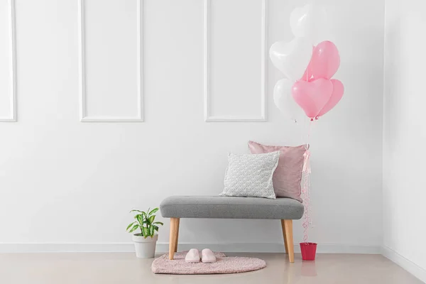 Grey bench with cushions and heart-shaped balloons near white wall. Valentine\'s Day celebration
