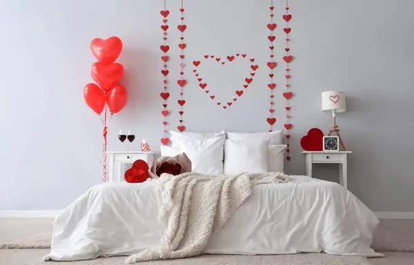 Interior of light bedroom with cozy bed, heart-shaped balloons and decorative hearts for Valentine's Day celebration