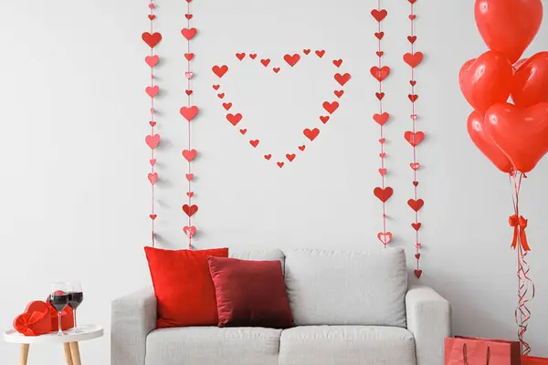 Interior of festive living room with grey sofa, heart-shaped balloons and decorative hearts. Valentine\'s Day celebration