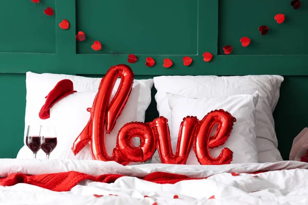 Cozy bed with glasses of wine and word LOVE made from balloons. Valentine\'s Day celebration
