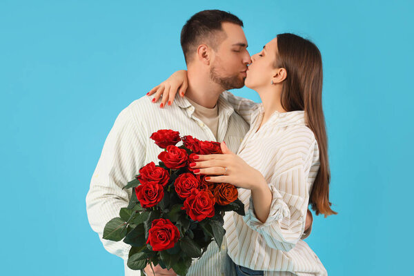 Lovely couple with bouquet of roses kissing on blue background. Valentine's Day celebration