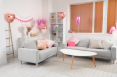 Gri koltukları, kalp şeklinde balonları ve sehpanın üzerinde güller olan şenlikli oturma odasının bulanık görüntüsü. Sevgililer Günü kutlaması