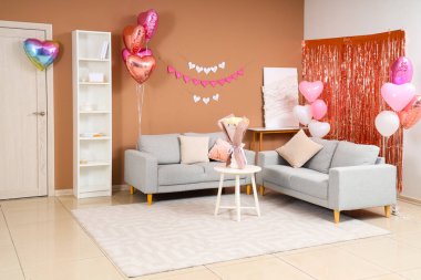 Gri koltukları, gül buketi ve kağıt kalpli çelenkleri olan şenlikli bir oturma odası. Sevgililer Günü kutlaması