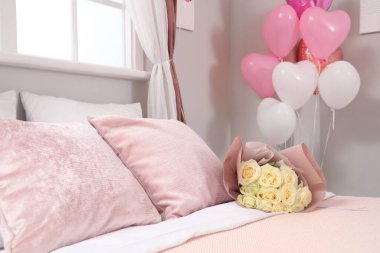 Şenlikli yatak odasının içinde kalp şeklinde balonlar ve yatakta güller. Sevgililer Günü kutlaması