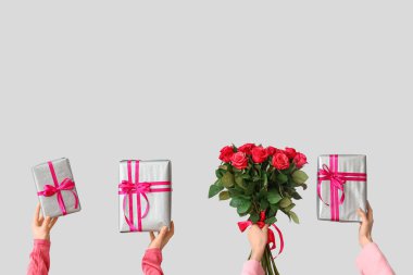 Hediye kutularıyla kadın elleri ve gri arka planda kırmızı güller. Sevgililer Günü kutlaması