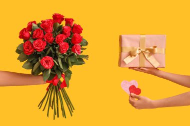 Hediye kutusu, kupa ve sarı arka planda kırmızı güller olan kadın elleri. Sevgililer Günü kutlaması