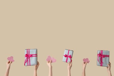 Hediye kutuları ve bej arka planda kalpleri olan kadın elleri. Sevgililer Günü kutlaması