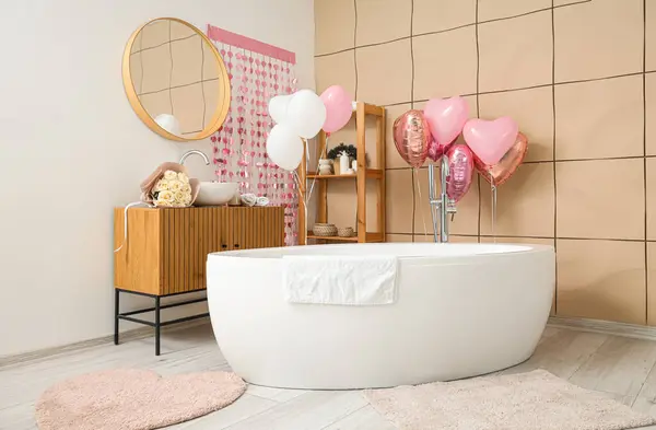 Interior of festive bathroom with bathtub, mirror and heart-shaped balloons. Valentine\'s Day celebration