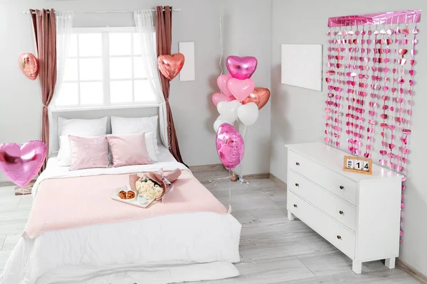 Interior of festive bedroom with heart-shaped balloons and bouquet of roses on bed. Valentine\'s Day celebration