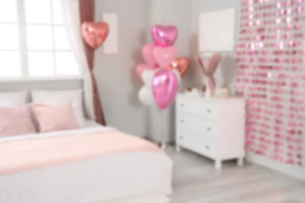 Blurred view of festive bedroom with heart-shaped balloons and cozy bed. Valentine's Day celebration