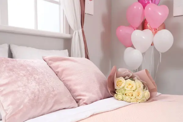 Interior of festive bedroom with heart-shaped balloons and bouquet of roses on bed. Valentine's Day celebration