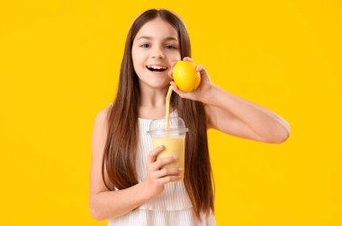 Sarı arka planda bir bardak smoothie ve limonlu küçük kız.