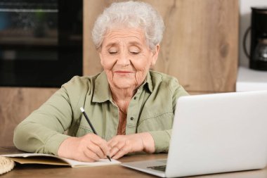 Mutfakta dizüstü bilgisayarı ve defteri olan son sınıf öğrencisi kadın.