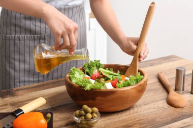 Mutfaktaki masada lezzetli salata ile zeytinyağı ekleyen bir kadın.