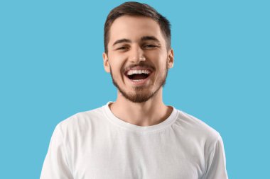 Mavi arka planda sağlıklı dişleri olan yakışıklı bir genç. Diş sağlığı konsepti