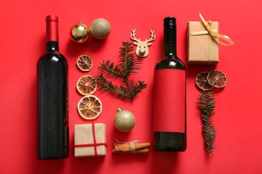 Kırmızı arka planda Noel ağacı dalları, toplar ve hediye kutuları olan bir şişe şarap.
