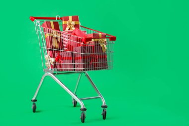 Noel hediyeleriyle dolu alışveriş arabası yeşil arka planda.