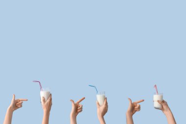 Açık mavi arkaplanda süt bardaklarını gösteren eller