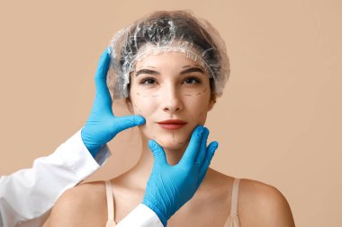 Yüzü işaretli genç bir kadın ve plastik cerrah. Bej arka planda, yakın plan.