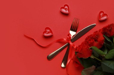 Fiyonklu çatal bıçak takımı, kırmızı arka planda mumlar ve güller. Sevgililer Günü kutlaması