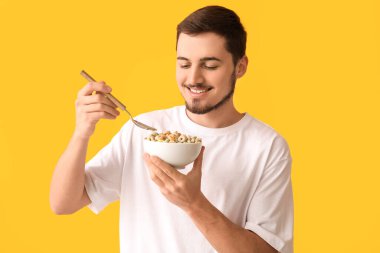 Handsome young man eating tasty cereal rings on yellow background clipart