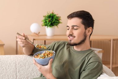 Yakışıklı genç adam oturma odasında lezzetli mısır gevreği halkaları yiyor.