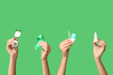 Kurdeleli, gözlüklü, kontak lensler için konteynır, yeşil arka planda cımbız ve göz damlası olan kadın elleri. Glaucoma farkındalık kavramı