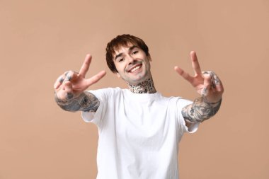 Yakışıklı genç adam bej arka planda zafer jesti gösteriyor.