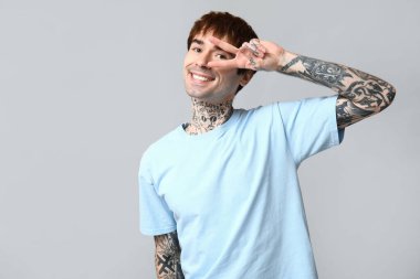 Yakışıklı genç adam gri arka planda zafer jesti gösteriyor.