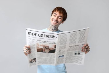 Gri arka planda gazetesi olan yakışıklı bir genç.