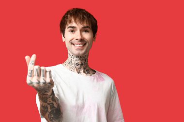 Kırmızı arka planda parmaklarıyla kalp yapan yakışıklı genç adam.