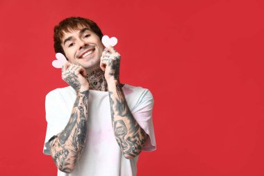 Kırmızı arka planda kağıt kalpli yakışıklı bir genç.