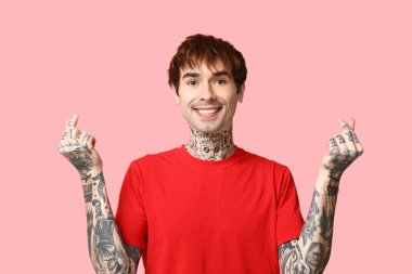 Yakışıklı genç adam pembe arka planda parmaklarıyla kalp yapıyor.