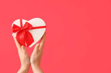 Kırmızı arka planda kalp şeklinde hediye kutusu tutan kadın elleri. Sevgililer Günü kutlaması