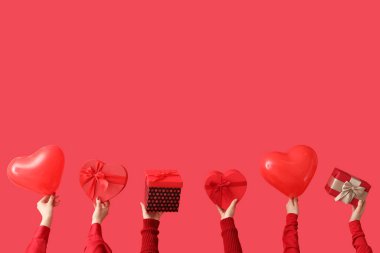 Kırmızı arka planda hediye kutuları ve kalp şeklinde balonlar tutan kadın eller. Sevgililer Günü kutlaması