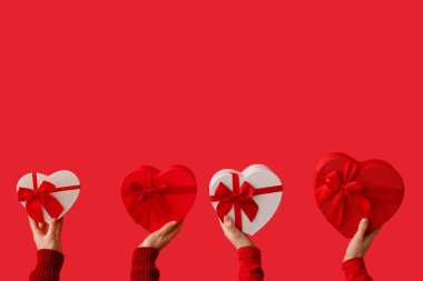 Kırmızı arka planda kalp şeklinde hediye kutularını tutan kadın elleri. Sevgililer Günü kutlaması