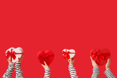 Kırmızı arka planda kalp şeklinde hediye kutularını tutan kadın elleri. Sevgililer Günü kutlaması