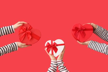 Kırmızı arka planda kalp şeklinde hediye kutularını tutan kadın elleri. Sevgililer Günü kutlaması