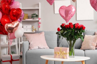 Oturma odasındaki sehpanın üzerinde bir buket güzel gül ve hediye kutusu olan vazo. Sevgililer Günü kutlaması