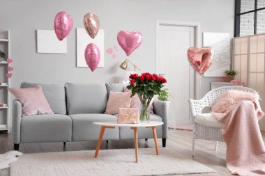 İçinde gri kanepe, kalp şeklinde balonlar ve sehpanın üzerinde güller olan şenlikli oturma odasının içi. Sevgililer Günü kutlaması
