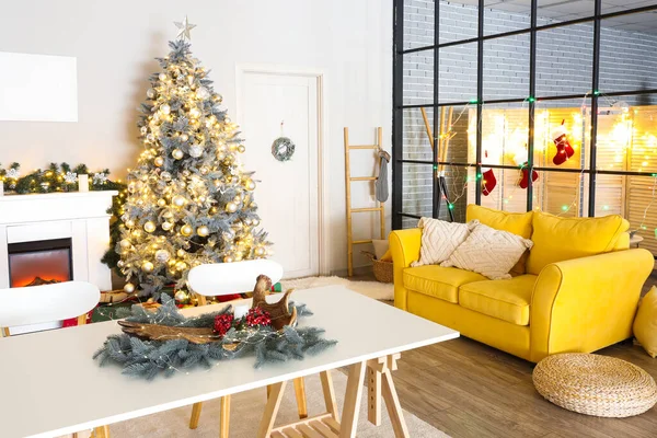 Interior of living room with yellow sofa, Christmas tree, fireplace and dining table